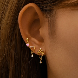 Close-up of gold S925 silver ear studs set with heart, chain, and crown designs