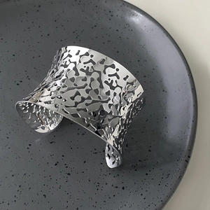 Macro detail of silver organic hollowed cuff bracelet on a matte textured ceramic tray