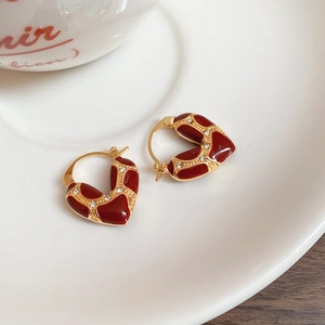 Detailed macro shot of heart-shaped gold earrings with red enamel and clear zircons