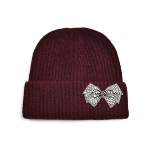 Détail d'un bonnet en tricot bordeaux foncé orné d'un grand nœud en strass brillants