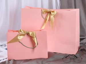 Detail of pink gift bags with golden ribbon handles in two sizes on soft fabric