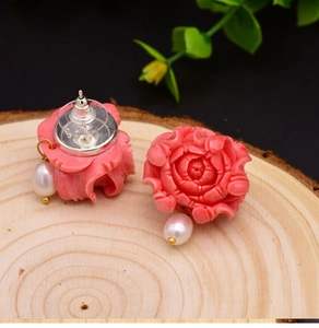 Detail view of pink rose stud earrings with white pearl pendants on a wooden background