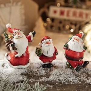 Three painted resin Santa Claus figurines displayed on snowy wood for Christmas decor