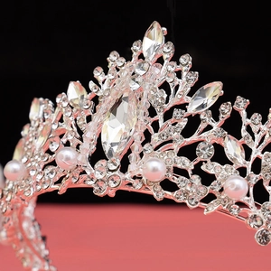 Close-up of silver bridal crown featuring white pearls and leaf-shaped crystals on red base