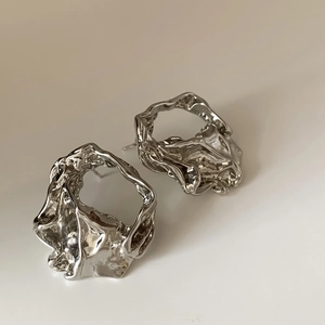 Macro detail of silver U-shaped earrings featuring a molten texture and mirror finish