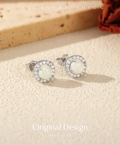 Close-up of S925 silver opal stud earrings with halo cubic zirconia on beige sand