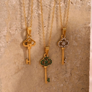 Close-up of three gold key pendants with green crystal, pearl, and polished finishes