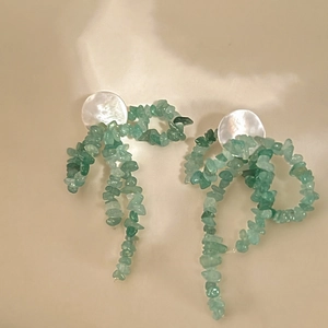 Détail de boucles d'oreilles pendantes avec pierres vertes et clous en nacre