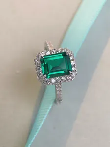 Macro detail of emerald-cut green gemstone ring with halo diamond setting in silver