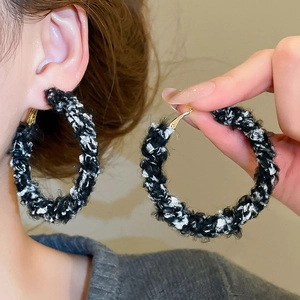 Détail de boucles d'oreilles créoles tricotées noir et blanc avec finition métal doré