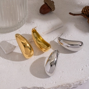 Detailansicht der tropfenförmigen Ohrstecker in Gold und Silber auf Steinhintergrund