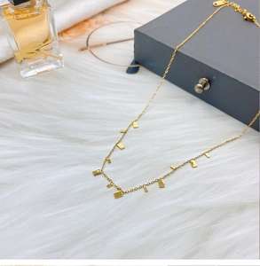 Detail of gold water-drop chain necklace with rectangular pendants on white plush fabric