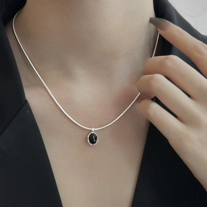 Macro shot of silver snake chain and black octagonal stone pendant on model neck