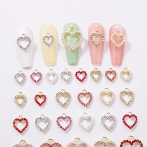 Detailed view of hollow heart nail charms with rhinestones and pearls on white background