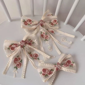 Detailed embroidery on white lace bow hair clips featuring pink flowers and green leaves