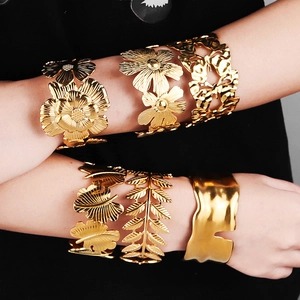 Detailed close-up of chunky gold cuff bracelets featuring floral and leaf metal patterns