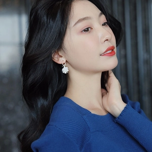 Close-up of floral drop earrings with white petals and diamond-studded hoops on a model