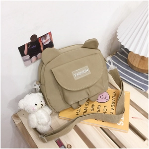 Detail of khaki canvas shoulder bag with cute bear ears and plush charm on wood shelf