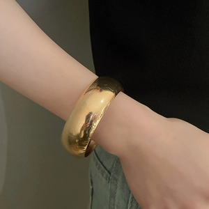 Detail showing irregular gold textured metal bangle on wrist with a minimalist design