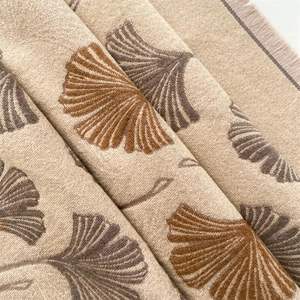 Macro detail of beige scarf fabric texture with brown ginkgo leaves and soft tassels