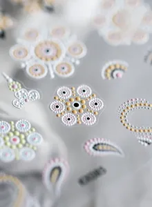 Vista macro di adesivi per unghie 3D con motivi geometrici floreali color crema