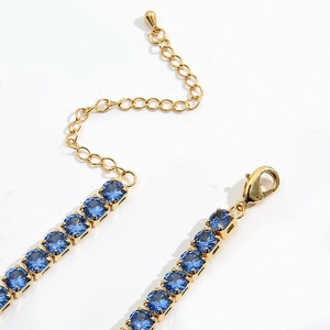 Macro detail of gold necklace featuring square blue zircon stones and lobster clasp closure