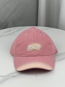 Detail of pink vintage baseball cap featuring white heart embroidery and distressed ripped holes