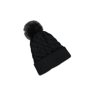 Close-up of black cable-knit winter hat with textured yarn and large faux fur pom-pom