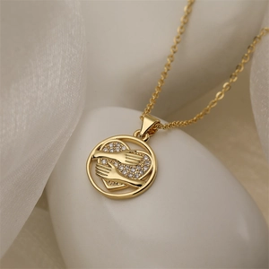 Macro shot of gold necklace pendant featuring two hands holding a sparkling heart