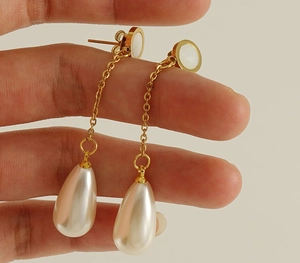 Detail of elegant 18K gold stainless steel drop earrings with shell inlay and pearl pendants