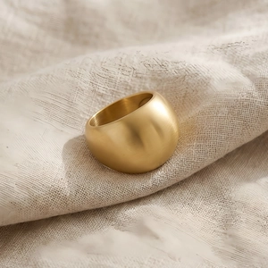 Macro detail of a wide matte gold stainless steel ring on beige linen fabric texture