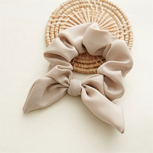 Detail of silk-like satin bow hair tie in beige resting on a woven rattan mat