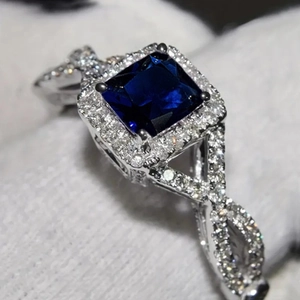 Détail d'une bague saphir bleu carré avec halo de diamants et anneau torsadé argenté