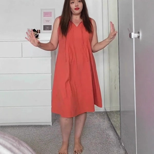 Detail of coral red pleated V-neck sleeveless dress featuring a relaxed A-line silhouette