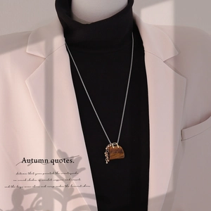 Silver necklace with brown handbag pendant on model wearing a beige blazer and black top