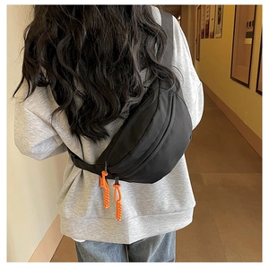 Detail of black canvas chest bag with orange zipper pull cords on adjustable shoulder strap