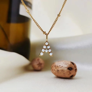Detail view of gold titanium steel necklace featuring a letter A pearl pendant