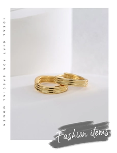Detailed macro shot of three-layer overlapping gold-plated hoop earrings on a minimalist base