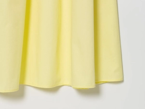 Detailed macro shot of light yellow poplin midi dress hemline with fine woven texture