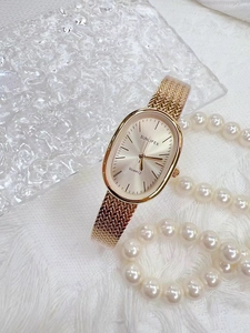 Elegant gold oval quartz watch with woven mesh strap on soft fabric with pearls