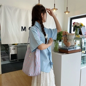 Detail of purple plaid canvas tote bag with pink bow accents on model in a cafe setting