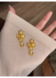 Close-up of golden floral earrings with zircons pinned on a beige knit sweater