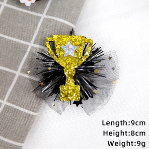 Detail of glittery gold trophy hair clip with silver star, black tassel and mesh