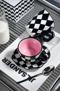Detail view of a checkered ceramic coffee cup set with a soft pink interior and matching saucer