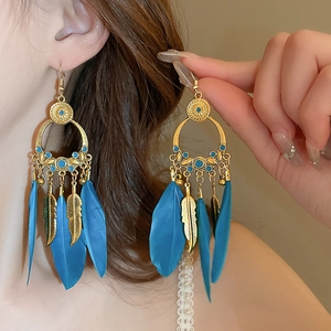 Detail view of Bohemian feather earrings featuring golden hoops and blue tassel details
