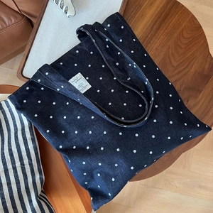 Détail du sac cabas en jean bleu à pois blancs avec écusson logo sur une table en bois