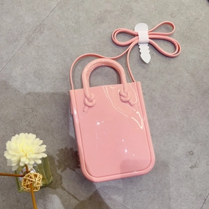 Pink PVC jelly tote bag with handles and shoulder strap on a grey concrete background