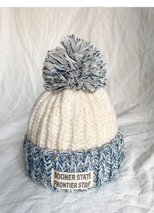 Close-up of knit winter hat featuring blue pom-pom and stitched text brand label