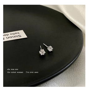 Macro detail of classic silver zircon stud earrings displayed on a dark matte plate