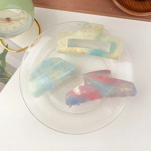 Detailed view of three iridescent star-colored hair claws in a transparent glass plate